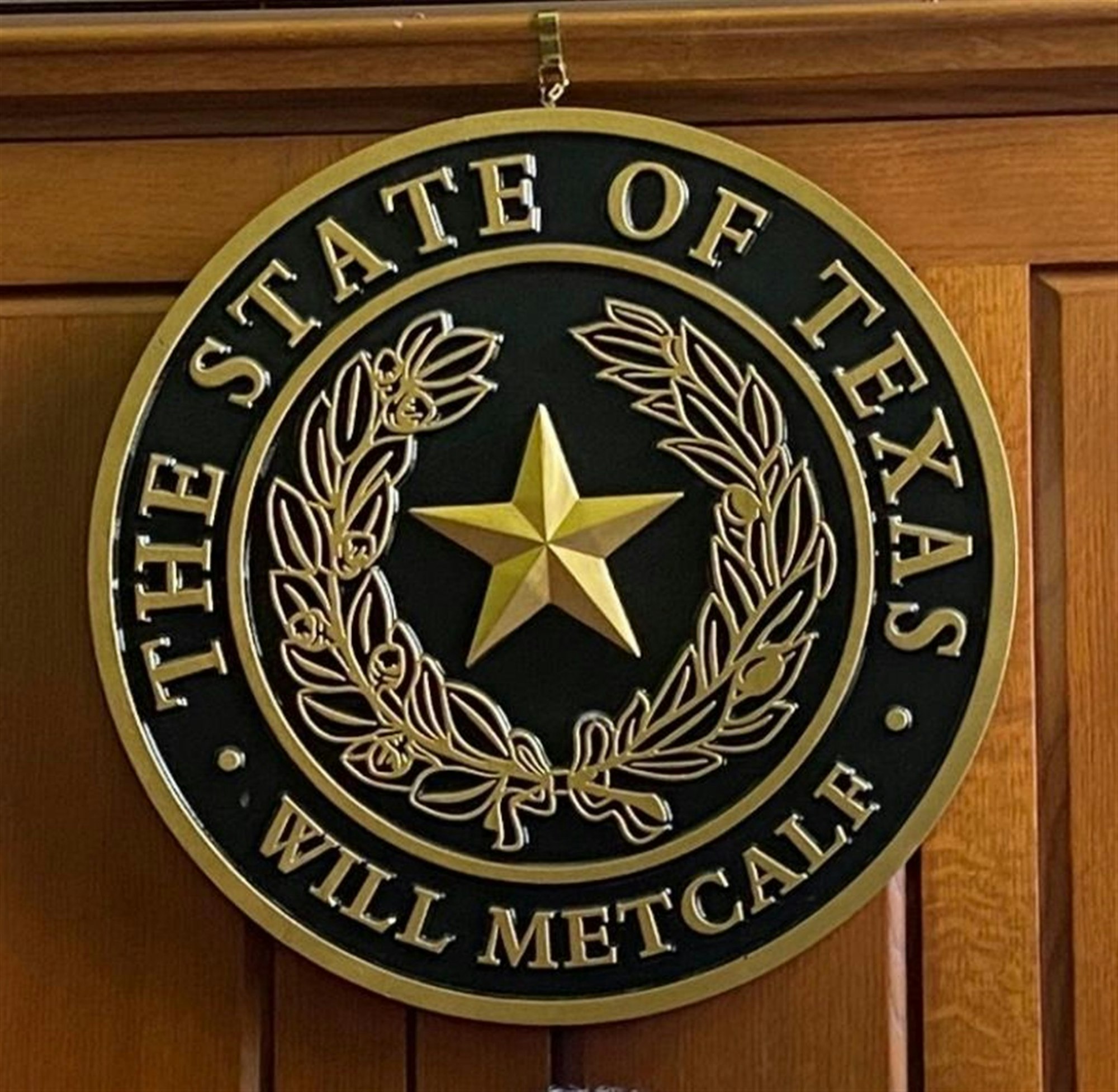 The image shows the seal of the State of Texas, featuring a star and laurel leaves, along with the name "Will Metcalf."