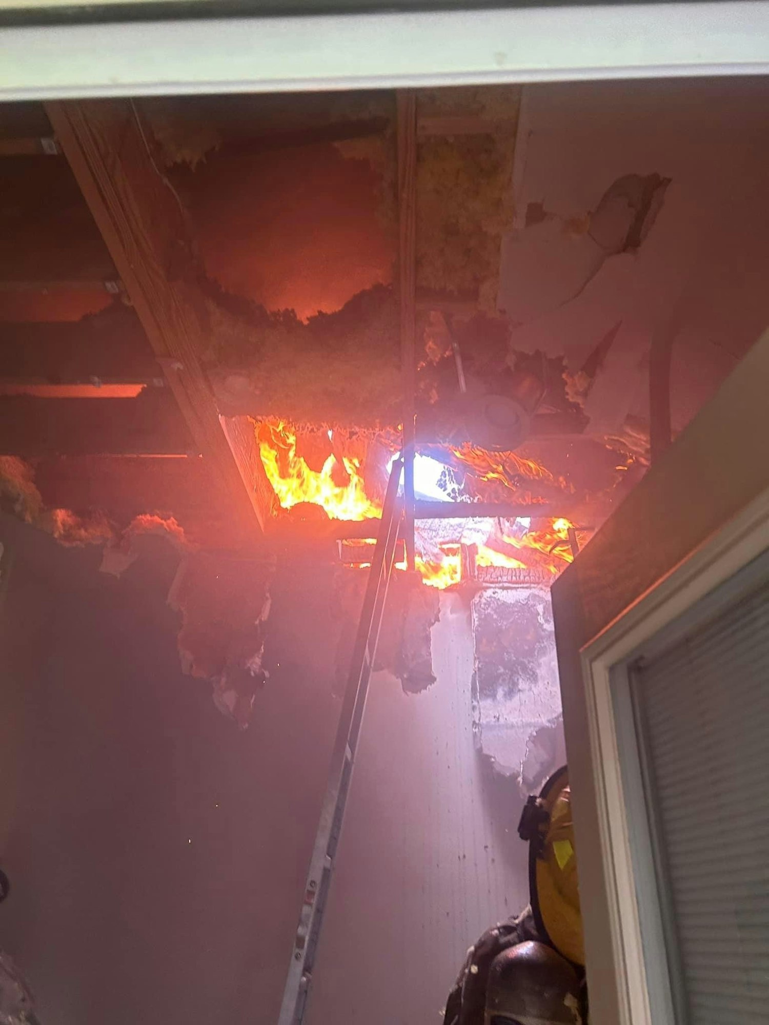 Firefighter inside a burning building, with visible flames and damaged ceiling.