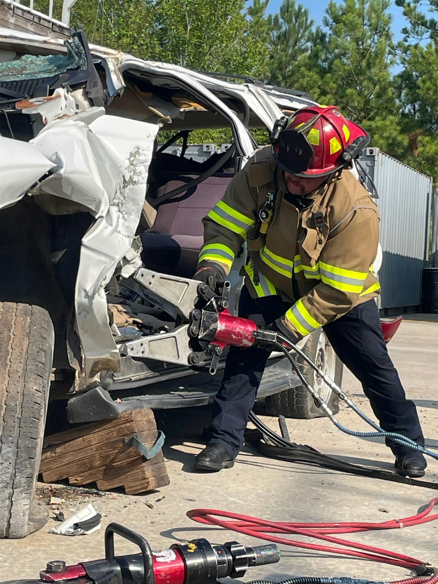 A firefighter uses hydraulic tools to rescue someone from a severely damaged vehicle in a training exercise.