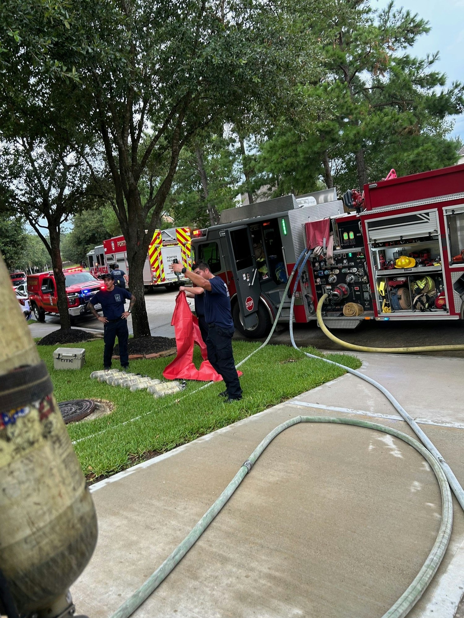 Firefighters and fire engines at a scene with hoses and equipment visible.