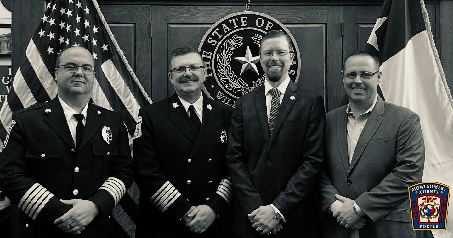 Four men posing in formal attire with U.S. and Texas flags in the background; Montgomery County Fire Rescue logo visible.