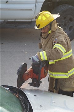 A firefighter in protective gear uses a cutting tool on a vehicle, creating sparks, likely during a rescue operation.