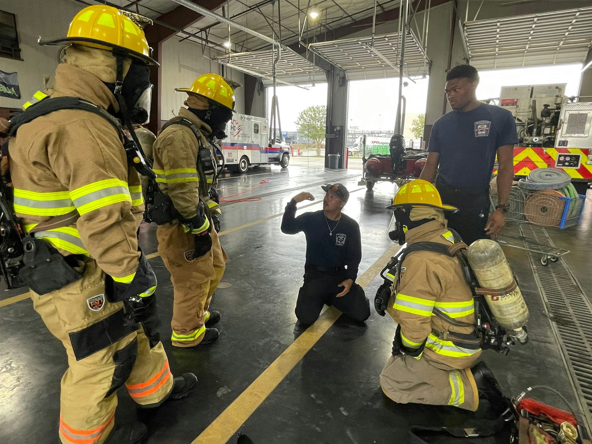 Firefighters in gear train or discuss while inside a fire station, showcasing teamwork and preparation for emergencies.
