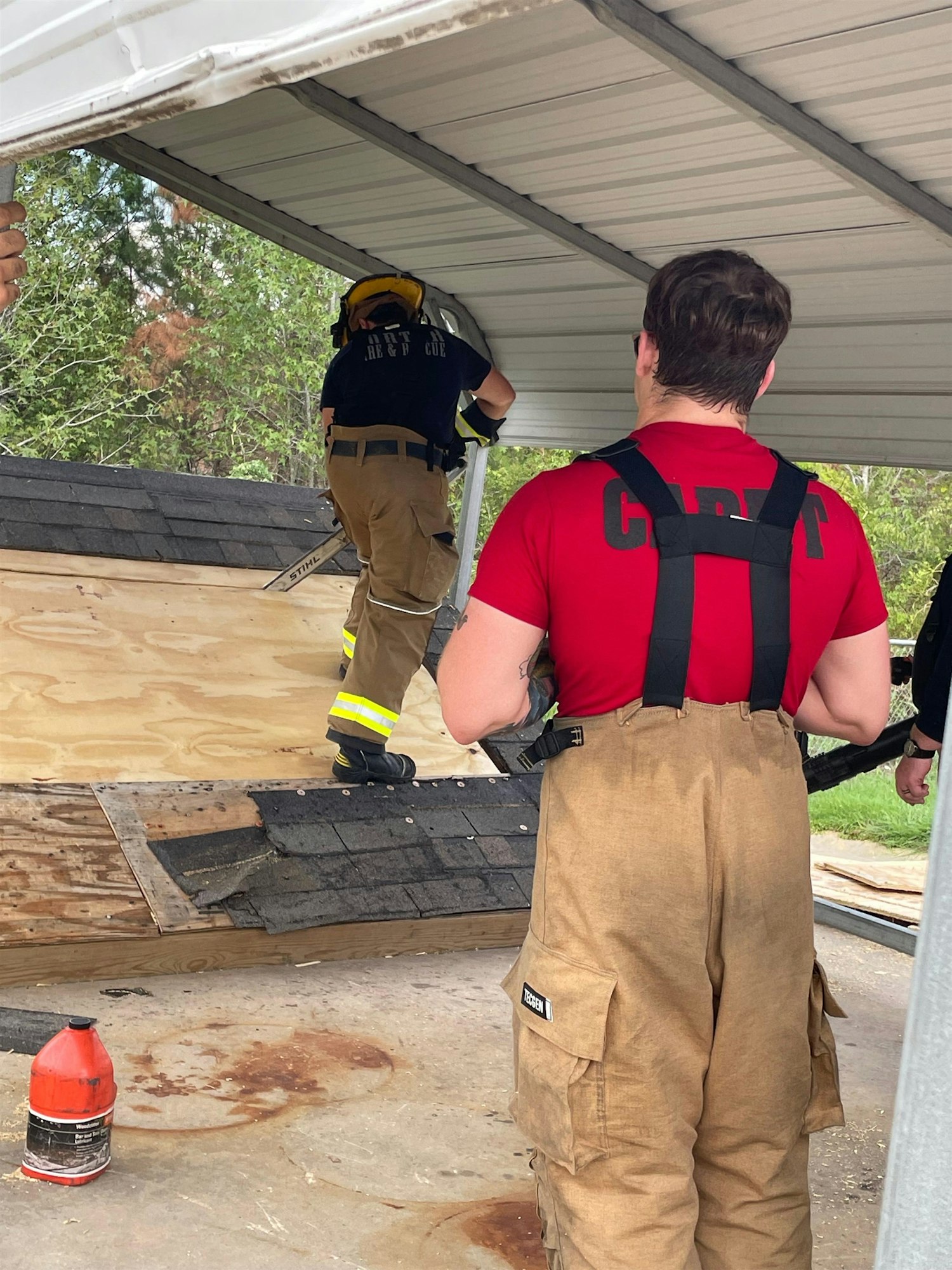 Firefighters are working on a roof, with one climbing while others assist, preparing for a task involving roofing materials.
