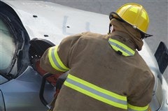 A firefighter in protective gear works on a vehicle, possibly involved in an accident or emergency situation.