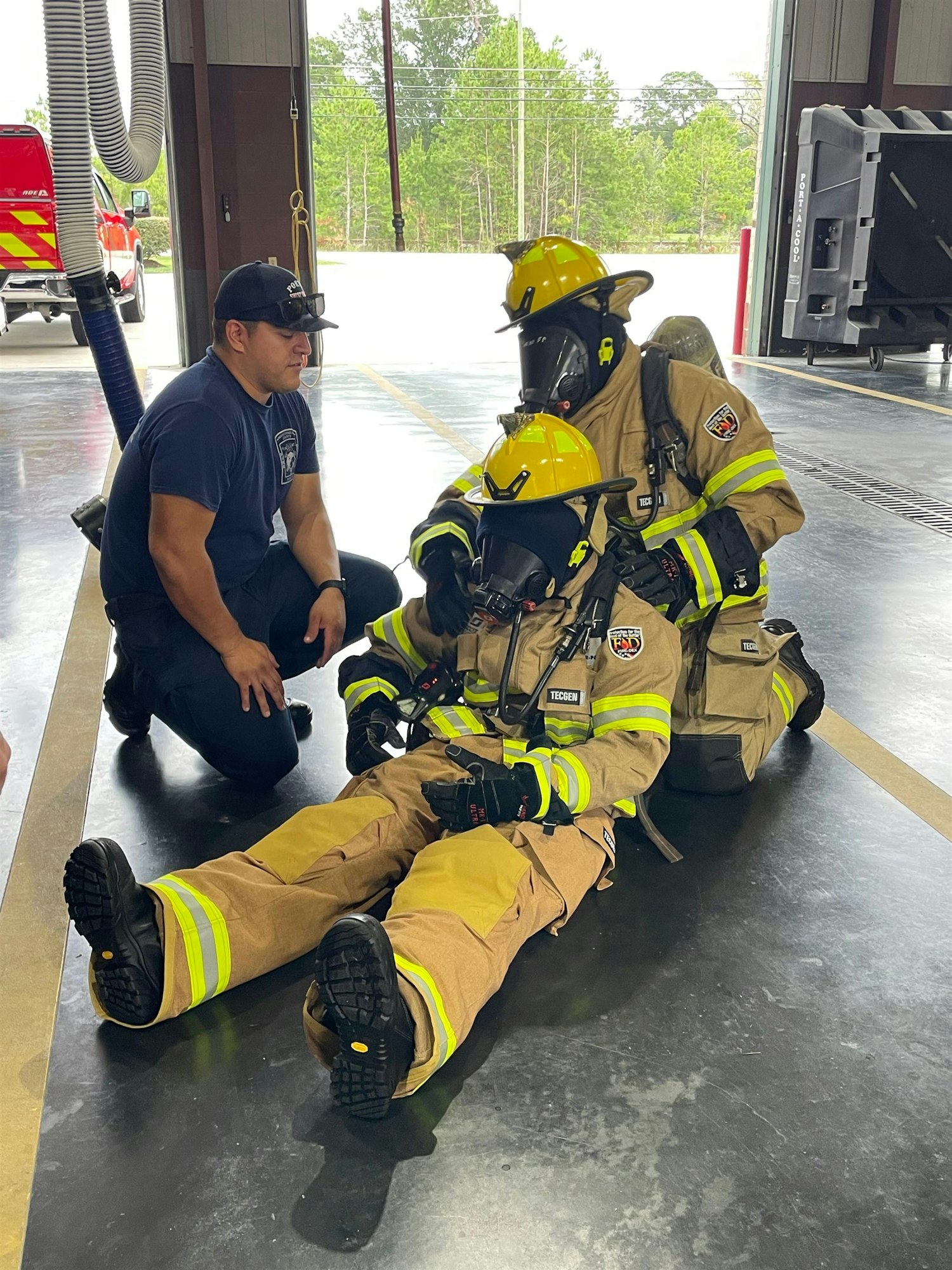 Three firefighters in gear are training or demonstrating a rescue technique, while a colleague observes and provides guidance.