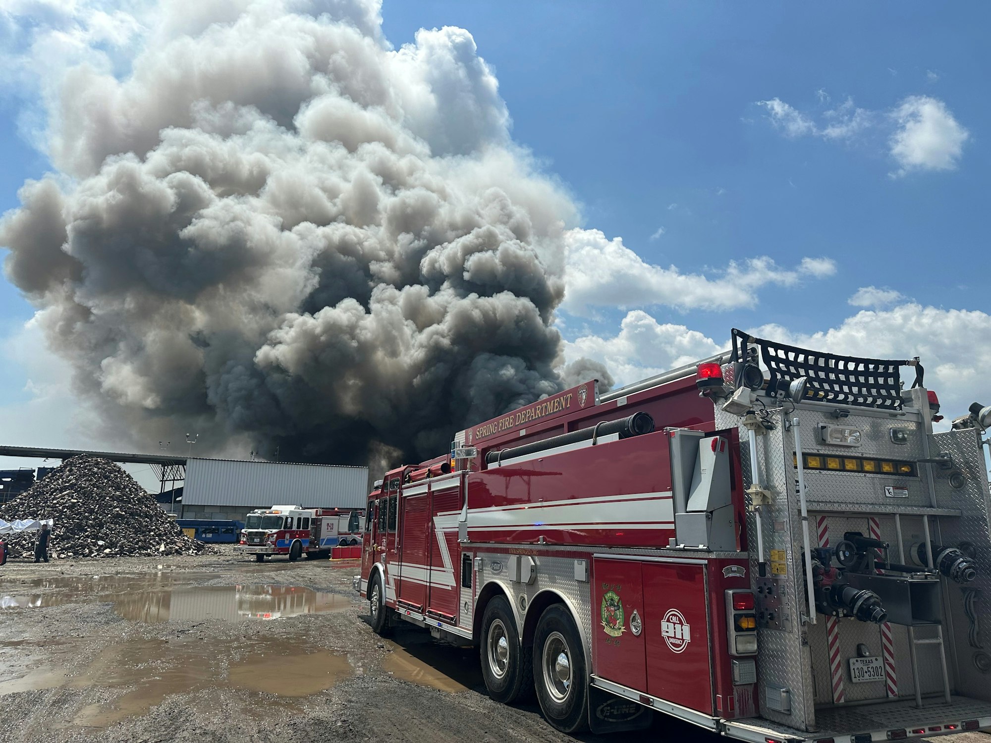 A fire truck at the scene of a large industrial fire with thick smoke.