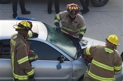 Firefighters are working on a silver car, using equipment to aid a rescue or manage an emergency situation.