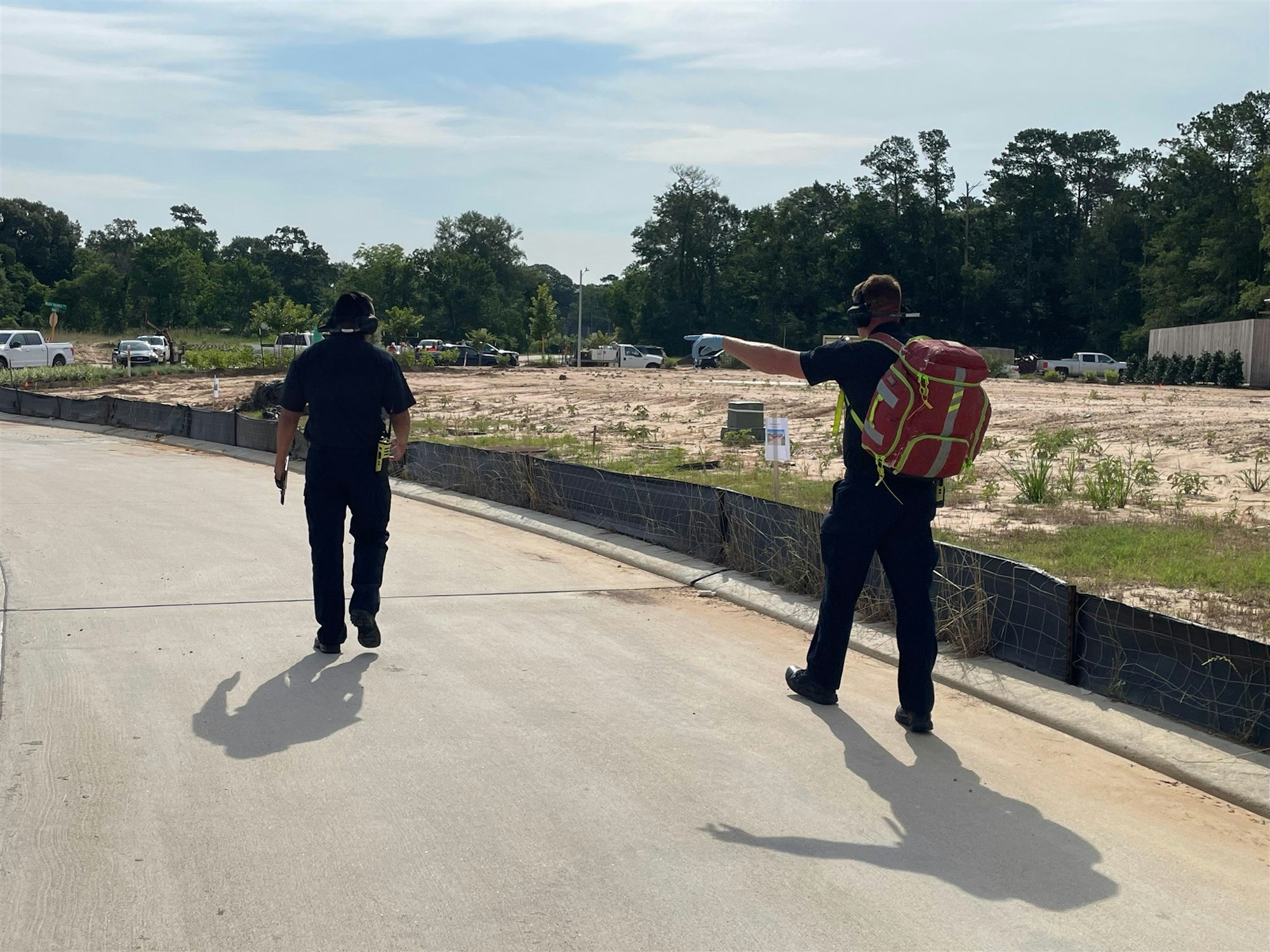 Two people walking in an open area, one pointing while carrying a large backpack, possibly engaged in a task or search.