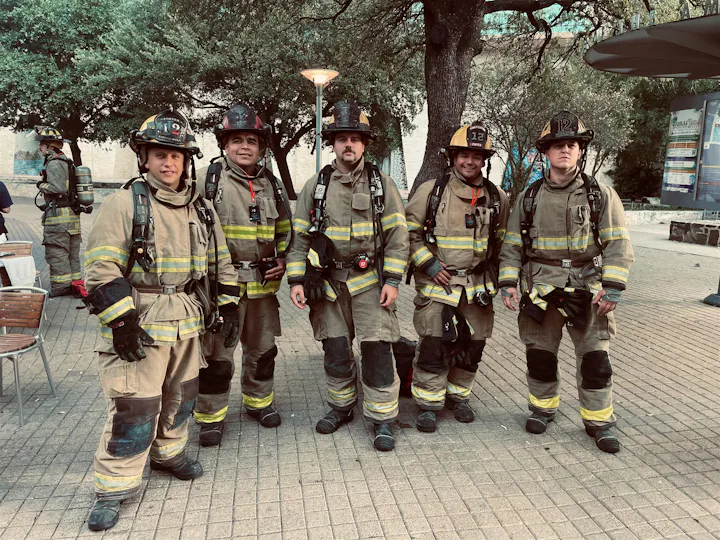 A group of five firefighters in full gear poses together outdoors, showcasing their uniforms and camaraderie.