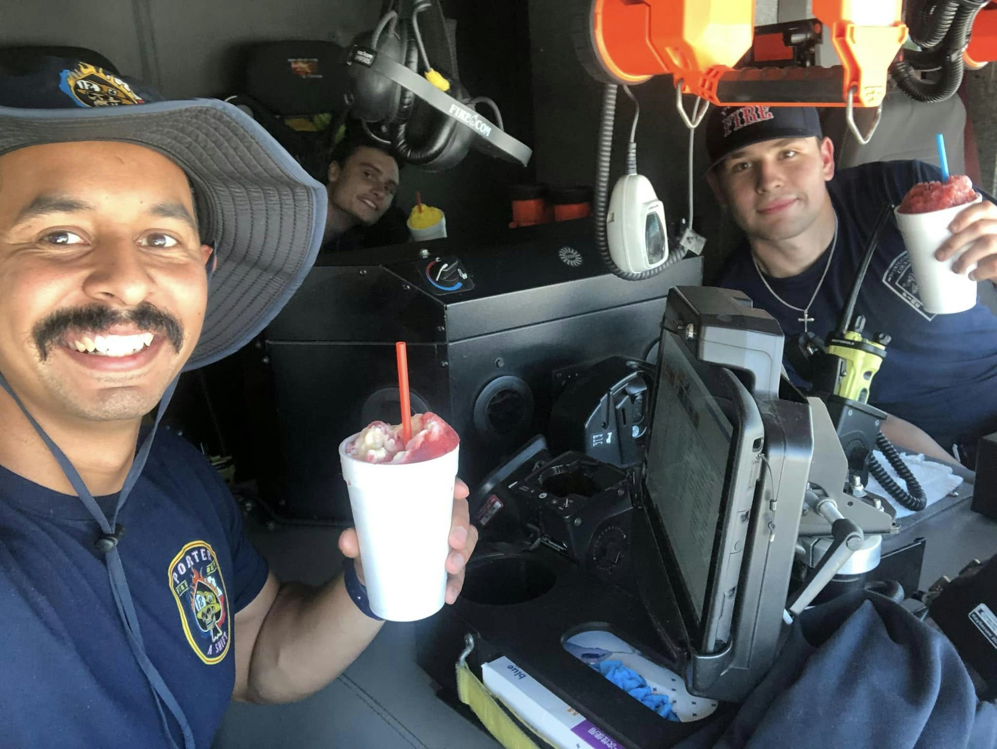 Firefighters inside a truck are smiling and enjoying icy treats, showcasing a moment of relaxation amidst their duties.