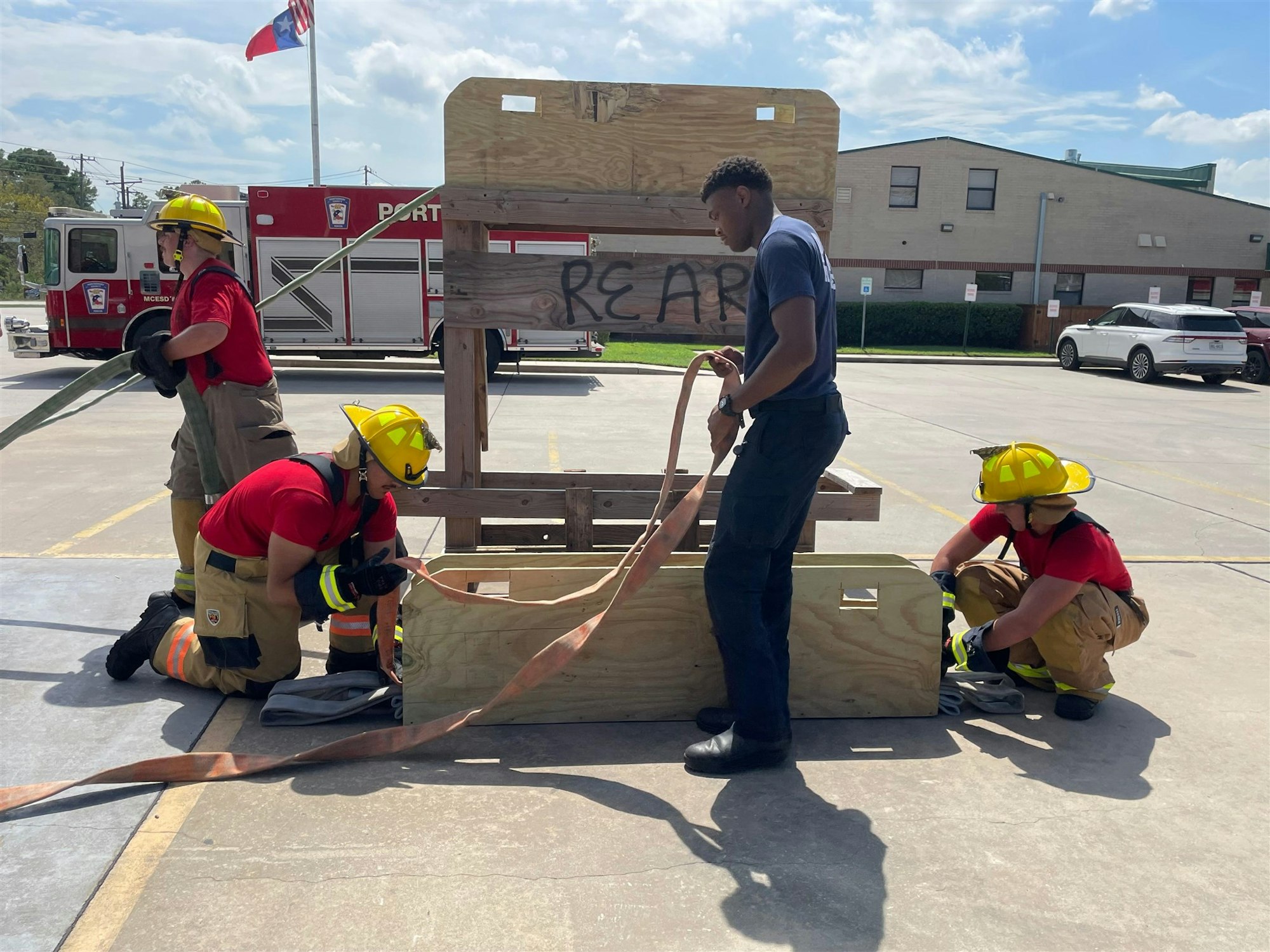 Firefighters are practicing equipment handling and teamwork on a training structure in a parking lot.