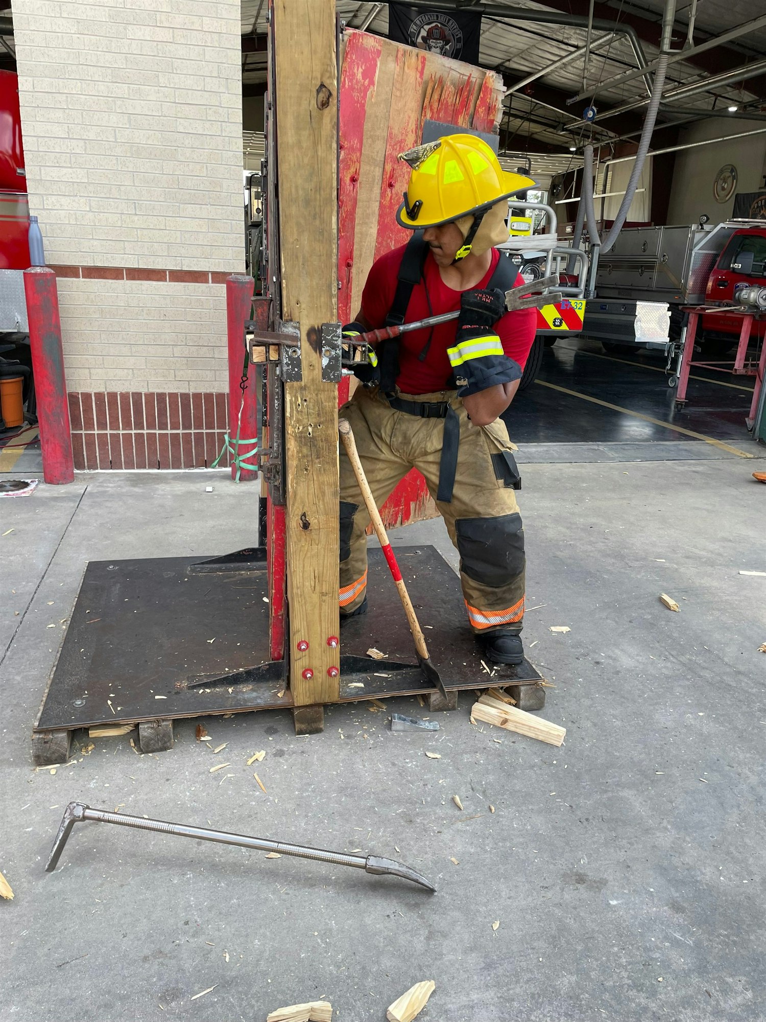 A firefighter in training uses tools on a wooden structure in a fire station, practicing breaching techniques.