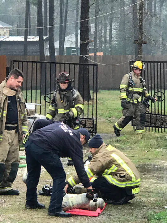 Firefighters work on a rescue operation, focusing on a situation involving safety equipment in a wooded area.