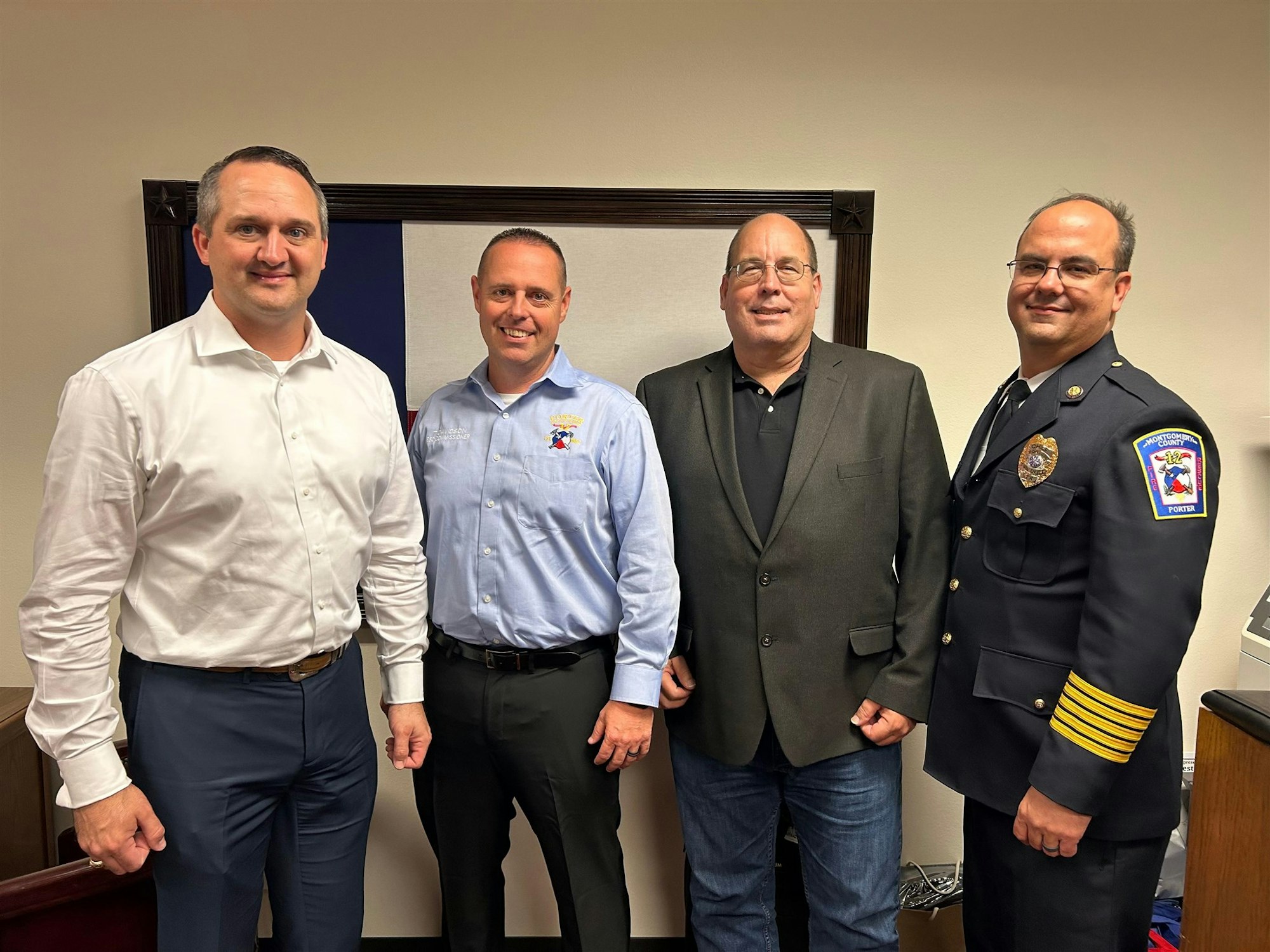 Four men posing together in a room, wearing business and police attire, with a Texas flag in the background.