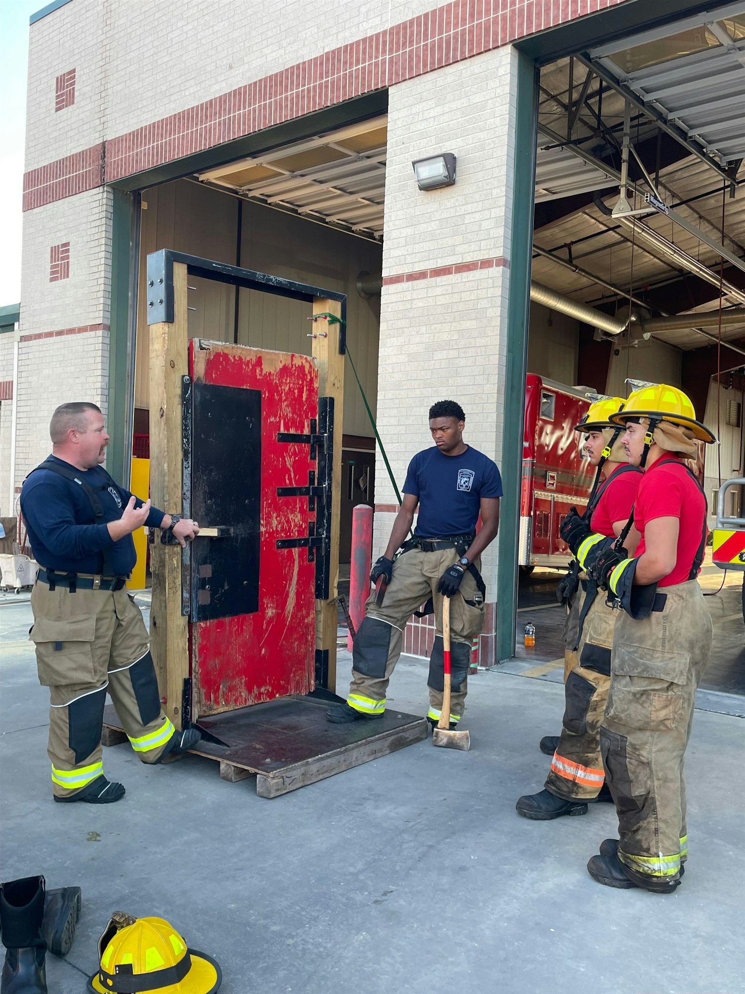 Firefighters are training with a simulated door, learning skills in a fire station setting.