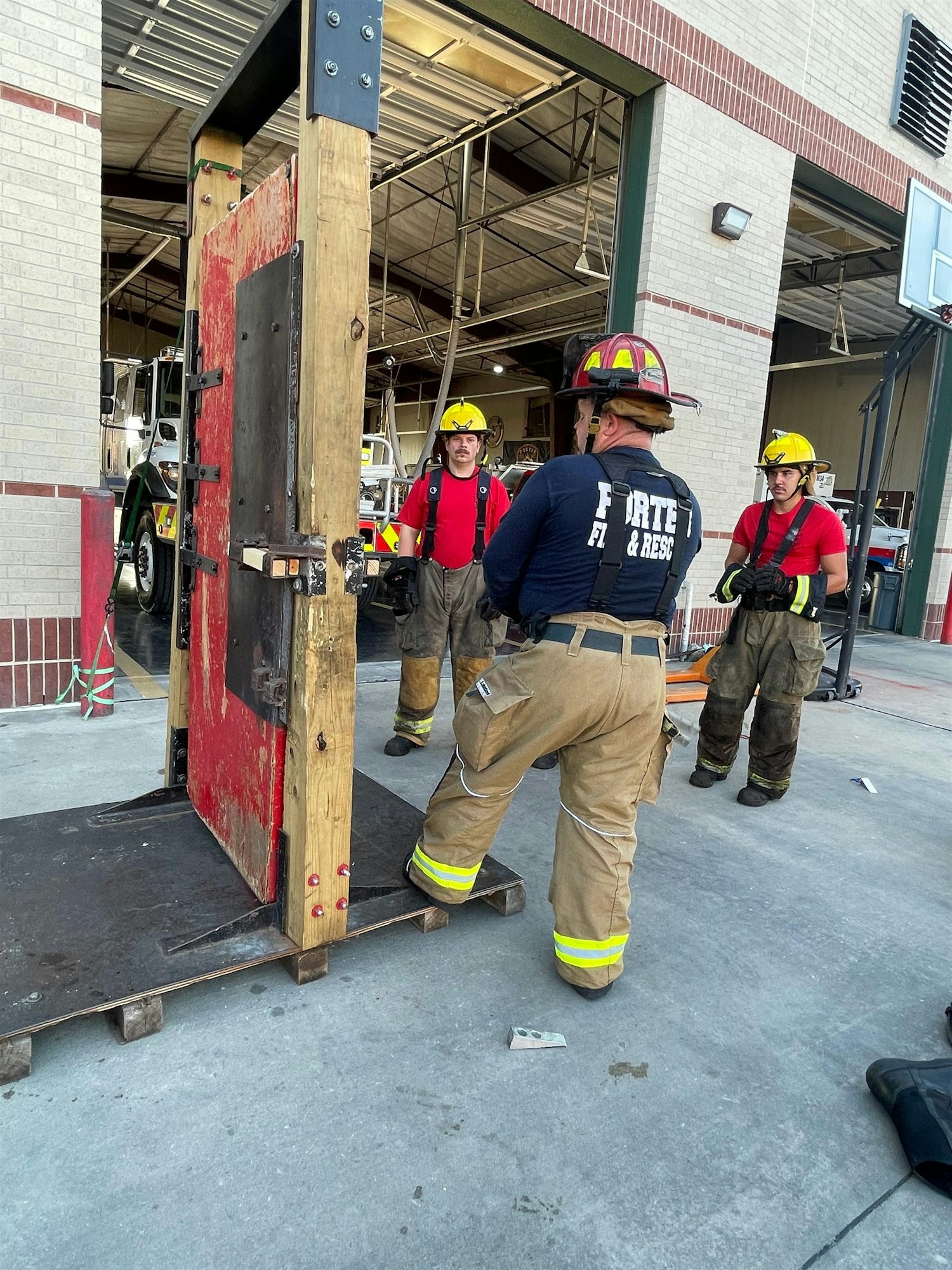 Firefighters are gathered around a training structure, preparing for drills in a fire station garage.