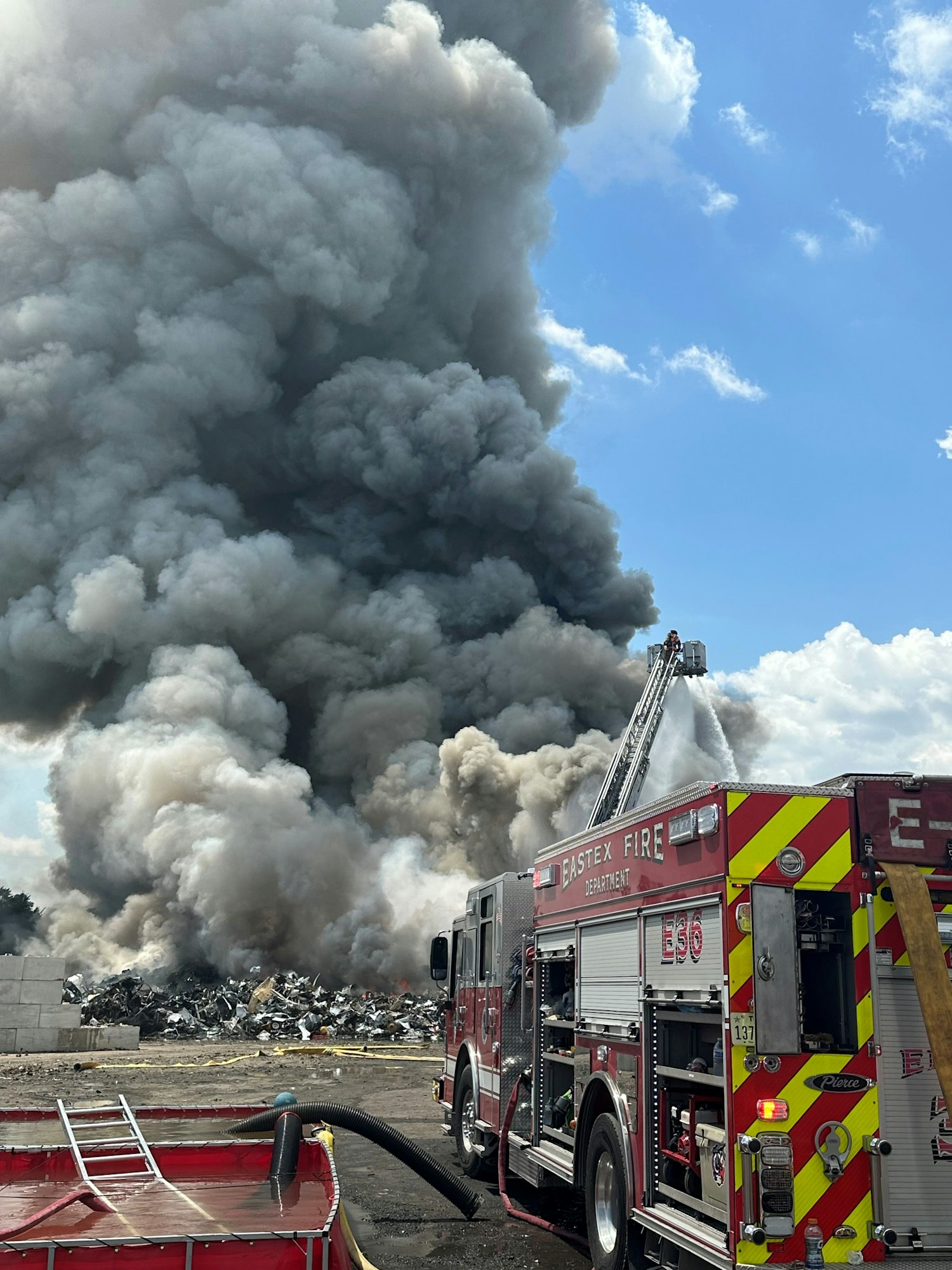 A fire truck sprays water on a large fire, with thick smoke rising into the sky.