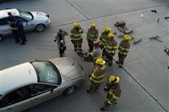 A group of firefighters gathers around a car, possibly conducting a training exercise or rescue operation.