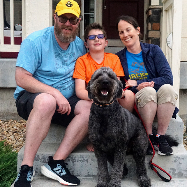 A family of three and their happy dog sitting on porch steps.