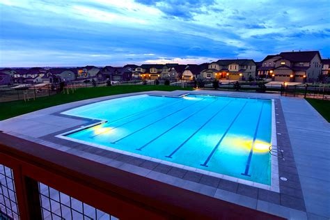 An illuminated outdoor swimming pool at dusk, with a residential backdrop.