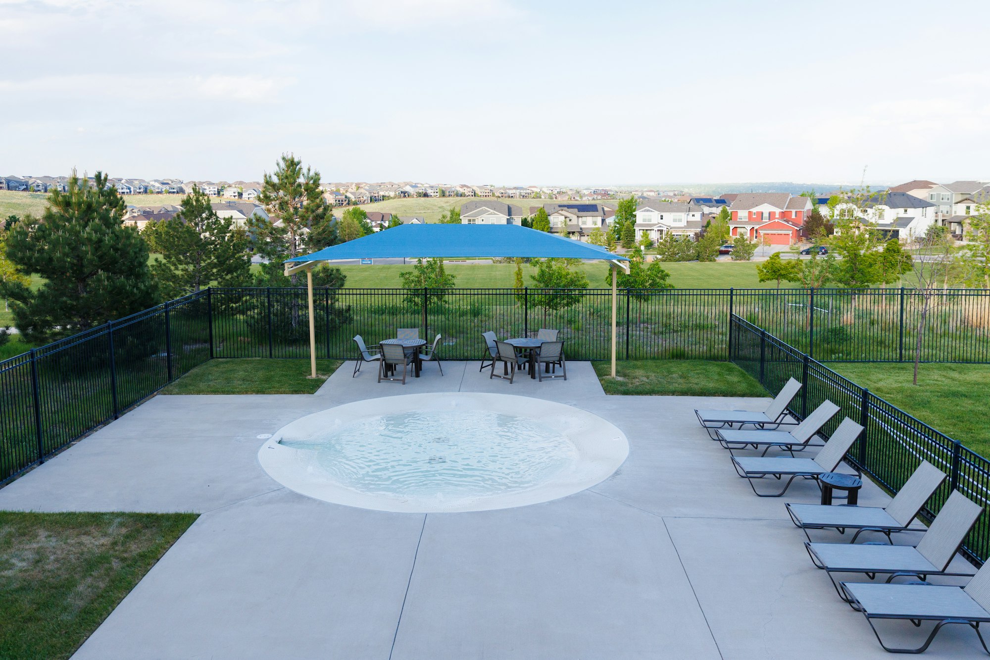 A pool area features lounge chairs, tables under a blue canopy, and scenic views of suburban homes and greenery.