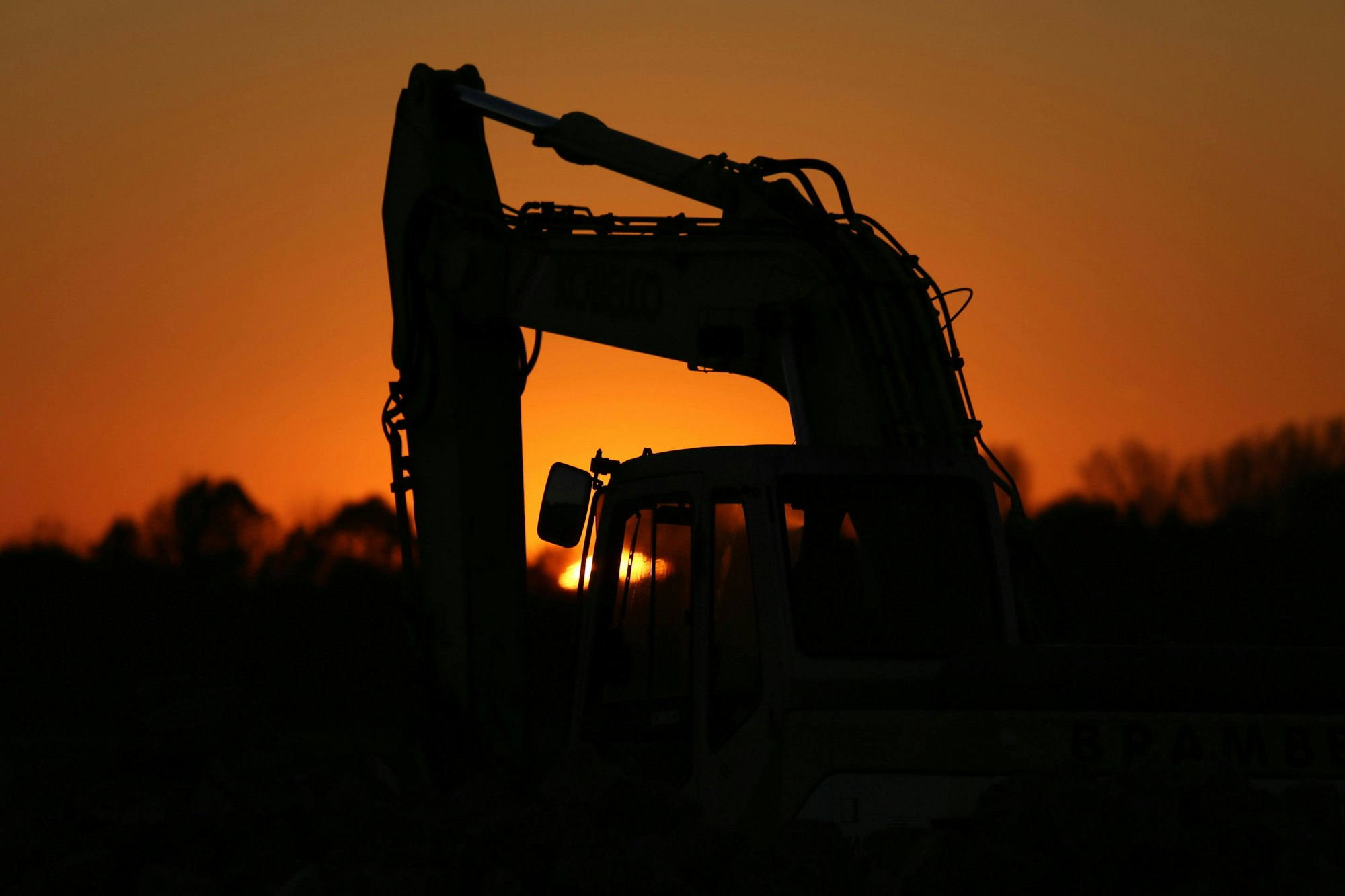 Silhouette of a construction excavator against a vibrant orange sunset sky.