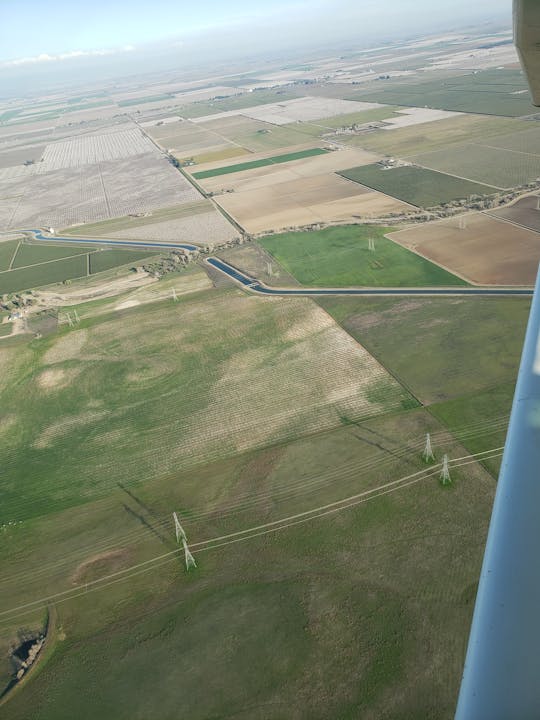 Aerial view of a patchwork of farmland, fields, and power lines, with a winding waterway cutting through the landscape.
