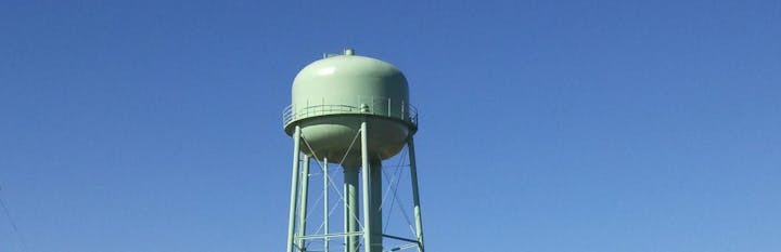 A green water tower stands against a clear blue sky.