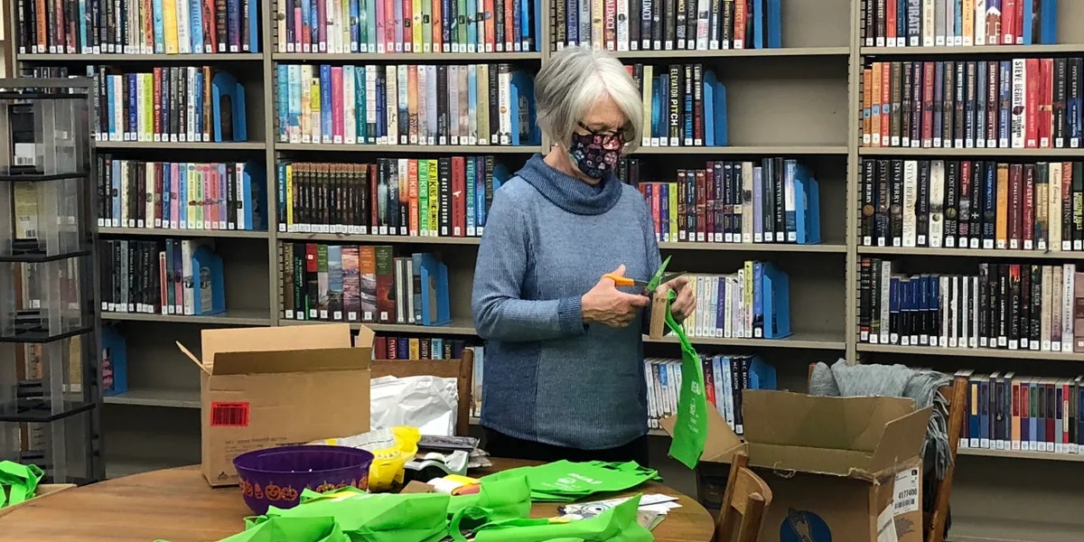 A person with scissors cutting fabric in a library surrounded by books.