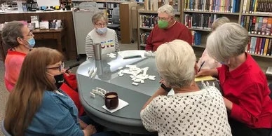 A group of people wearing face masks playing a game at a table in a library.