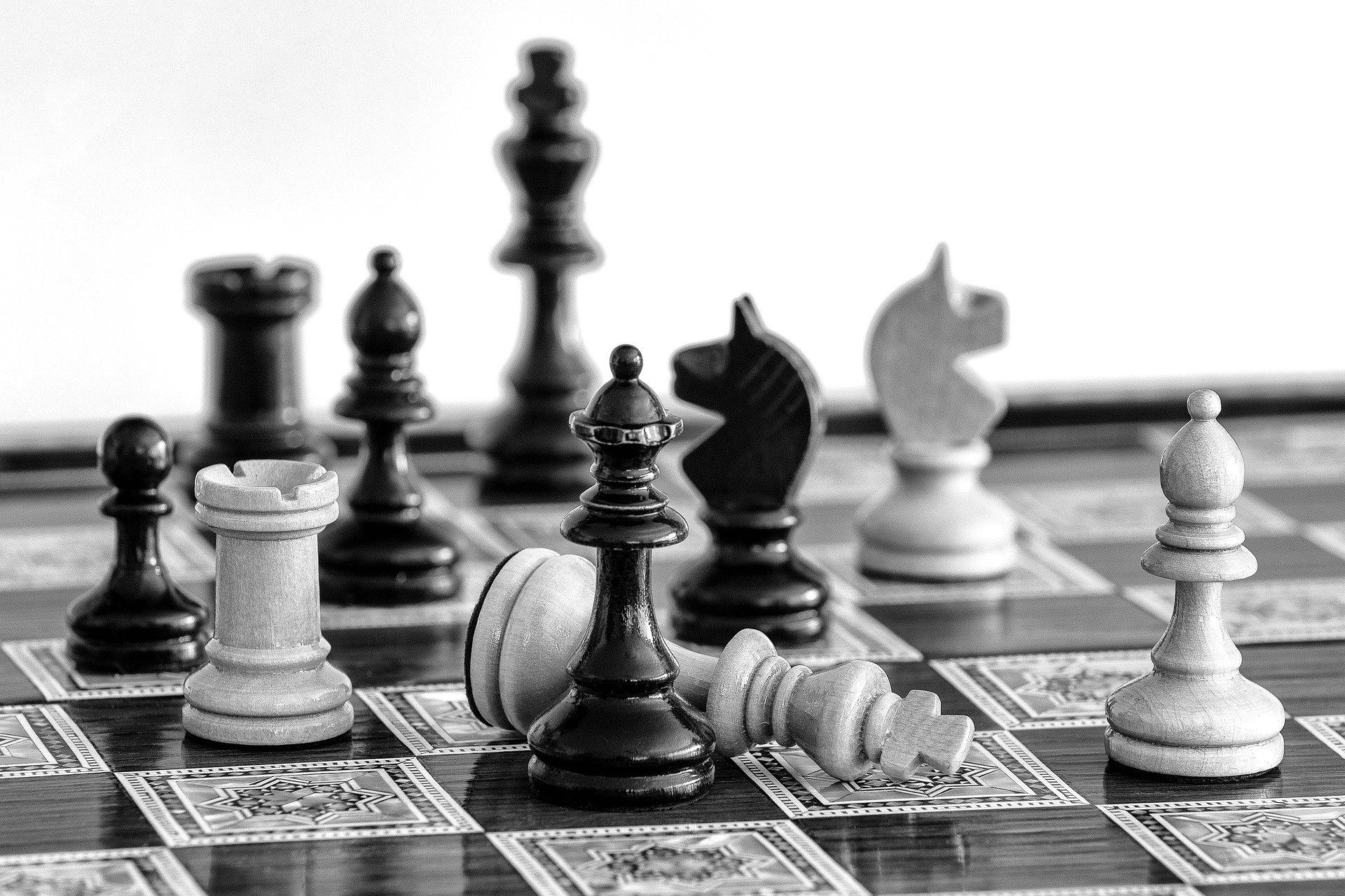 A black and white image of a chessboard, featuring various chess pieces, with one king toppled over.