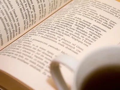 An open book with text and a cup of tea casting a shadow over the page.