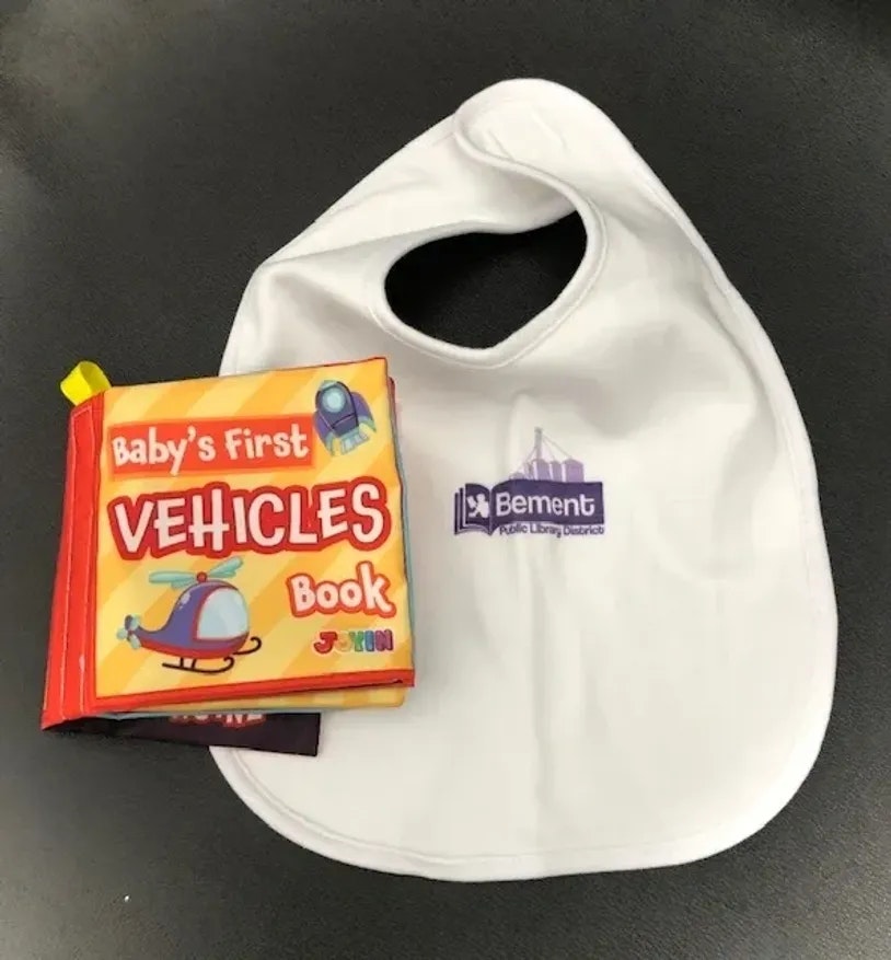 A baby's bib and a children's book titled "Baby's First VEHICLES Book" on a table.