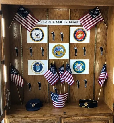 A display cabinet with military emblems, flags, and the text "WE SALUTE OUR VETERANS".