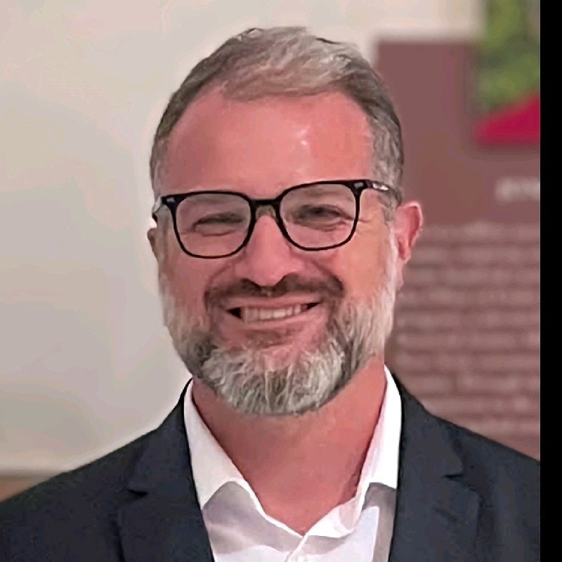 A smiling man with glasses, beard, and a suit.