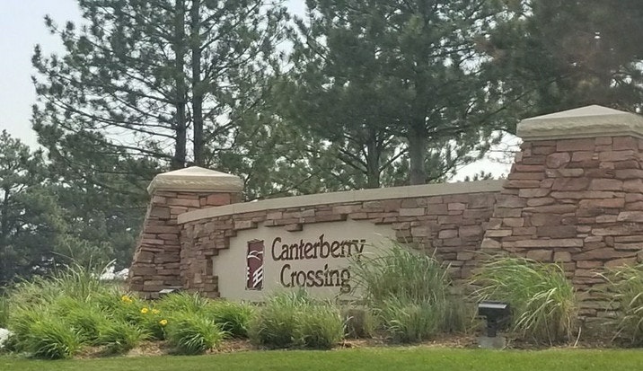 A stone sign for "Canterberry Crossing" with greenery and trees in the background.