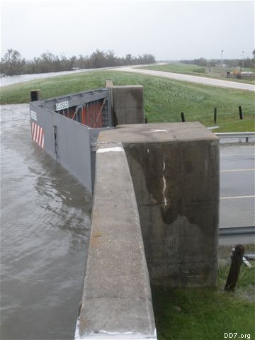 A floodgate is closed to block high water on a roadway near a river or canal, with "Closed" signs visible.