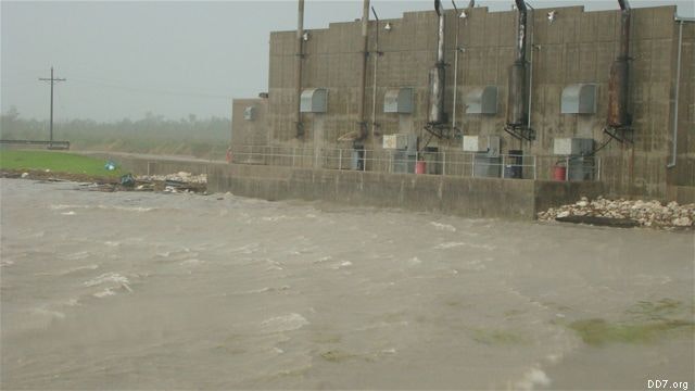 A concrete structure beside a turbulent body of water, possibly a flood.
