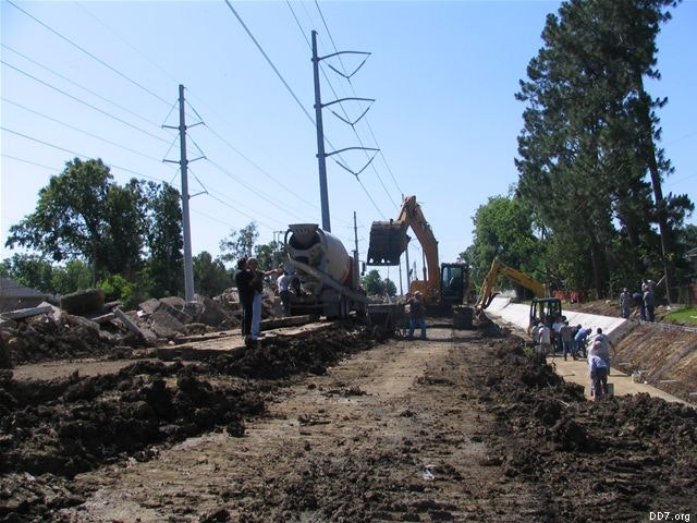 Construction site with heavy machinery, workers in hard hats, power lines, and trees.