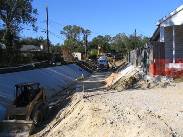 Construction site with heavy machinery and trucks working on a canal or drainage system in a residential area.
