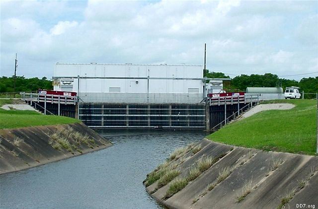 A white building behind a waterway with barriers and grassy banks on either side.