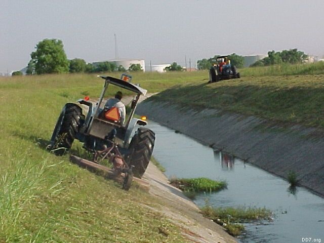 Two tractors mowing grass along the banks of a canal.