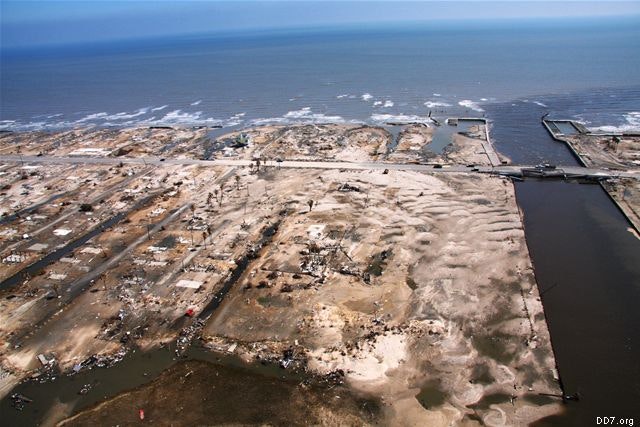 An aerial view of a coastal area with significant storm damage, debris, and flooded sections near the ocean.