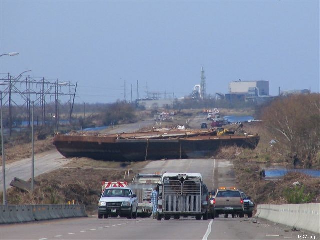 A large barge blocking a highway with several vehicles stopped in front.