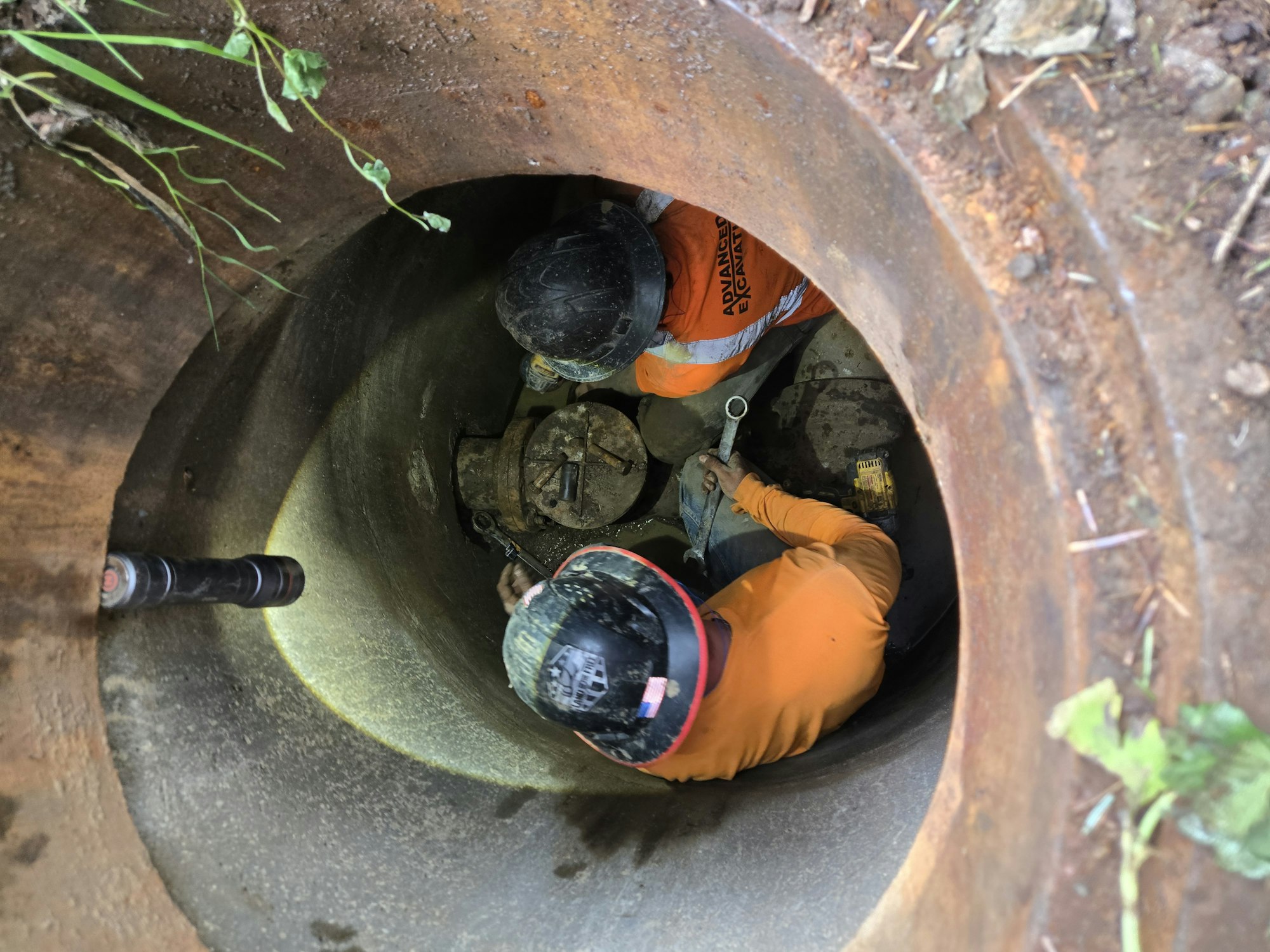 Two workers in safety gear inside a circular shaft, performing maintenance or repair work.