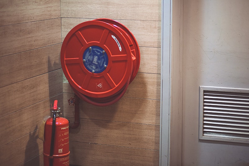 A red fire hose reel mounted on a wall next to a fire extinguisher.