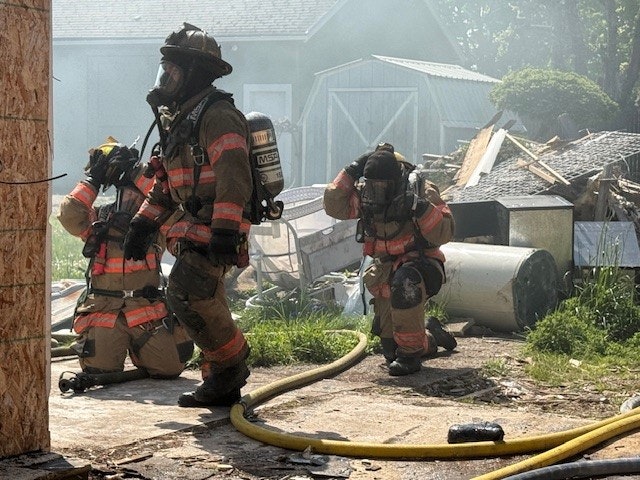 Firefighters in gear responding to a scene with smoke and debris, focused on managing a situation.