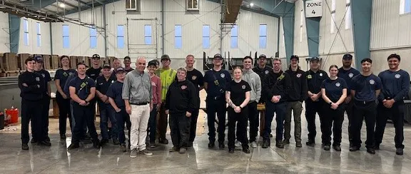 A group photo of people, likely a team or organization, standing in a large indoor space with the sign "Crooked Hop Farm."
