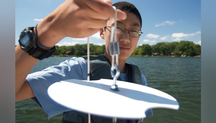 A person holding a Secchi disk on a boat near a body of water, used for measuring water clarity.